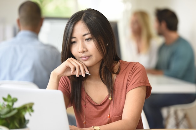 Mujer asiática joven de la raza mixta que trabaja en oficina