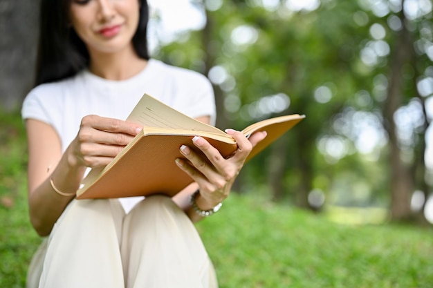 Mujer asiática joven relajada y tranquila con ropa informal leyendo un libro en el parque verde