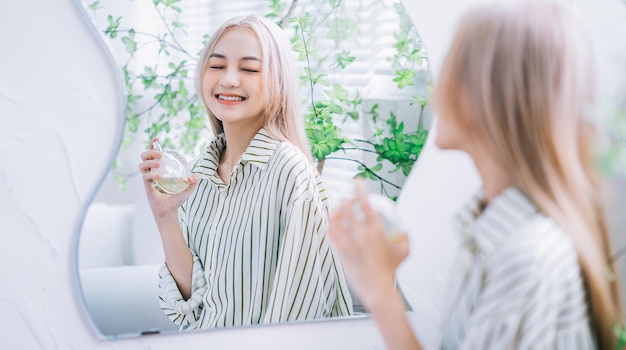 Mujer asiática joven rociando perfume frente al espejo