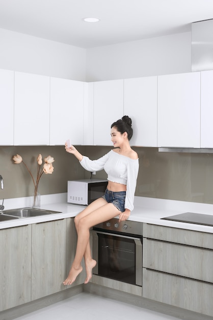 Mujer asiática joven sentada en la encimera de la cocina.