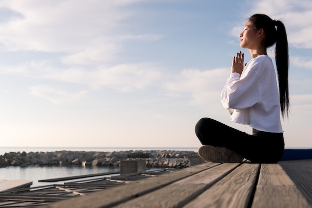 Mujer asiática joven sentada meditando junto al mar