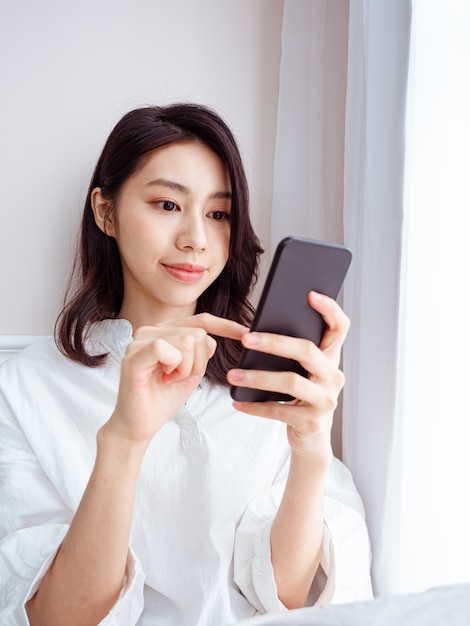 Mujer asiática joven con smartphone en casa
