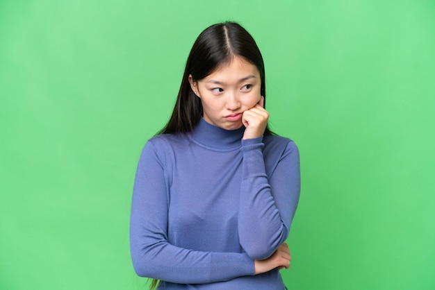 Mujer asiática joven sobre un fondo clave de croma aislado con expresión cansada y aburrida