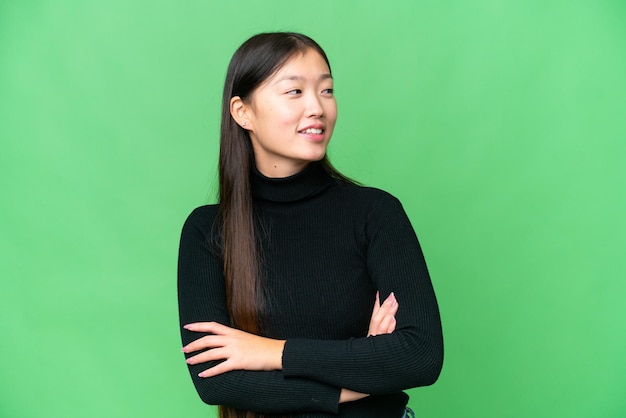 Mujer asiática joven sobre un fondo clave de croma aislado mirando hacia un lado