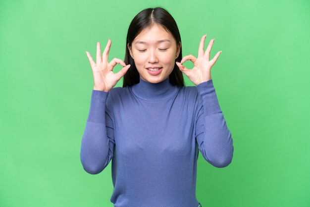 Mujer asiática joven sobre fondo clave de croma aislado en pose zen