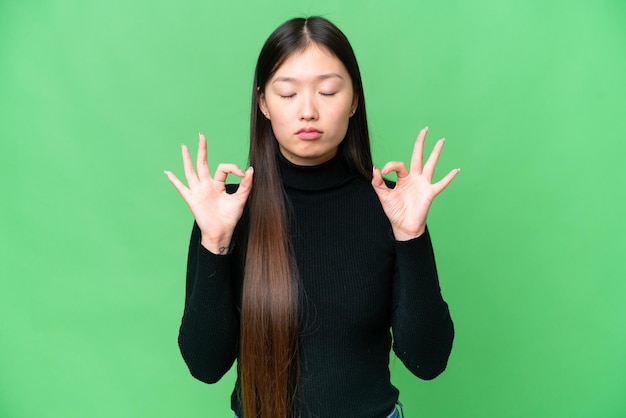 Mujer asiática joven sobre fondo clave de croma aislado en pose zen