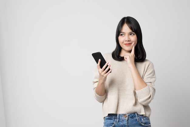 Mujer asiática joven sonriente que sostiene el smartphone que se coloca en fondo blanco aislado.