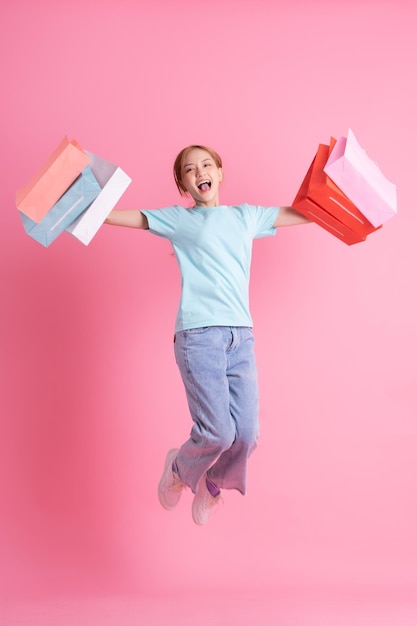 Mujer asiática joven sosteniendo bolsa de compras sobre fondo rosa