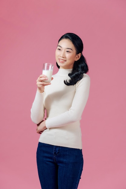 Mujer asiática joven sosteniendo leche con una sonrisa sobre fondo rosa