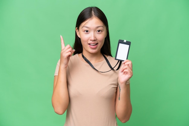 Mujer asiática joven con tarjeta de identificación sobre un fondo aislado que señala una gran idea