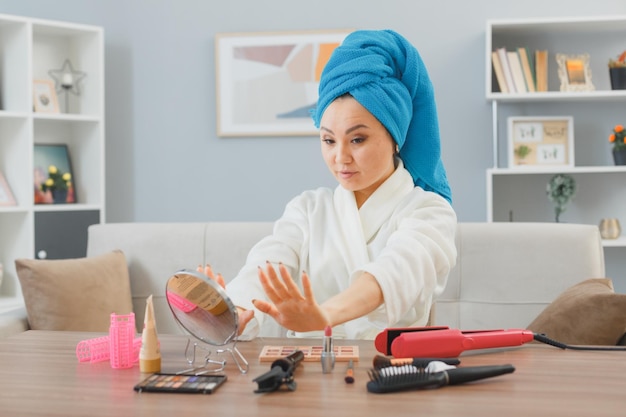 Mujer asiática joven con una toalla en la cabeza sentada en el tocador de su casa mirándose las uñas haciendo el concepto de belleza y cosmética facial de rutina de maquillaje matutino