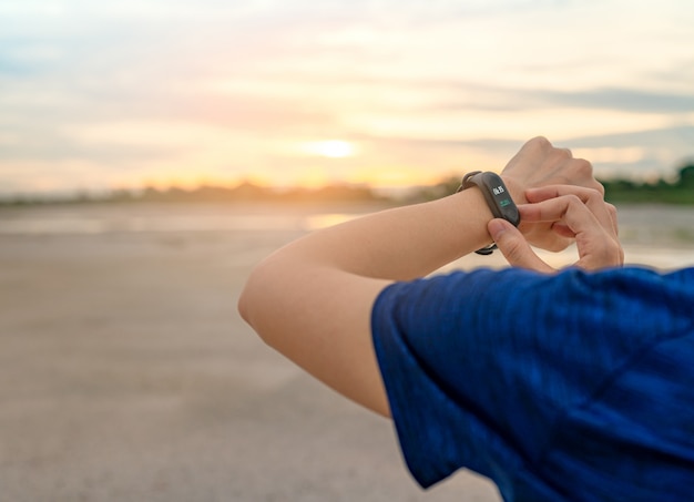 Mujer asiática joven tocando banda inteligente después de correr por la mañana. Computadora portátil. Pulsera de monitor de frecuencia cardíaca. Dispositivo de fitness. Rastreador de actividad o estado físico.