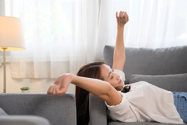 Mujer asiática joven tomando una siesta en el sofá en la sala de estar feliz concepto de estilo de vida saludable