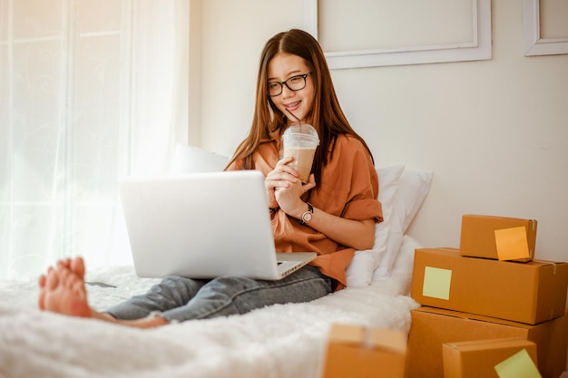 Foto mujer asiática joven trabaja desde casa hablando con los clientes para vender productos en línea y entregarlos al cliente. propietario de negocio, pyme, envío, trabajo desde casa (fmh), autónomo, concepto de puesta en marcha.