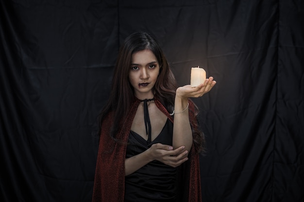 Mujer asiática joven en traje de bruja y vela sobre fondo de tela negra del concepto de Halloween. Retrato de mujer adolescente vestida como bruja para celebrar el festival de Halloween.