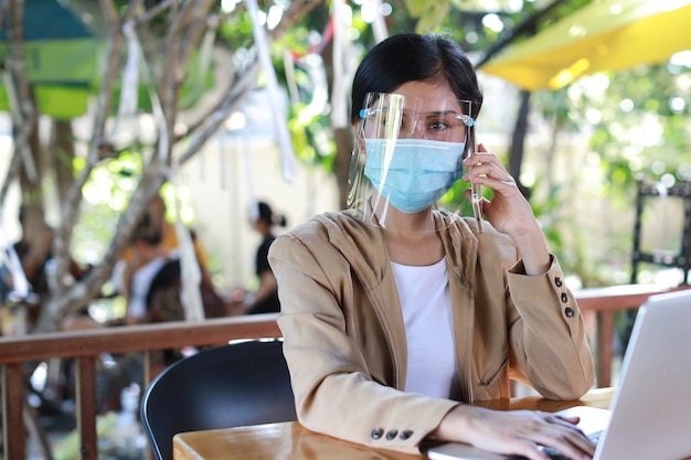 Mujer asiática joven en vestido casual con protector facial y máscara protectora para atención médica