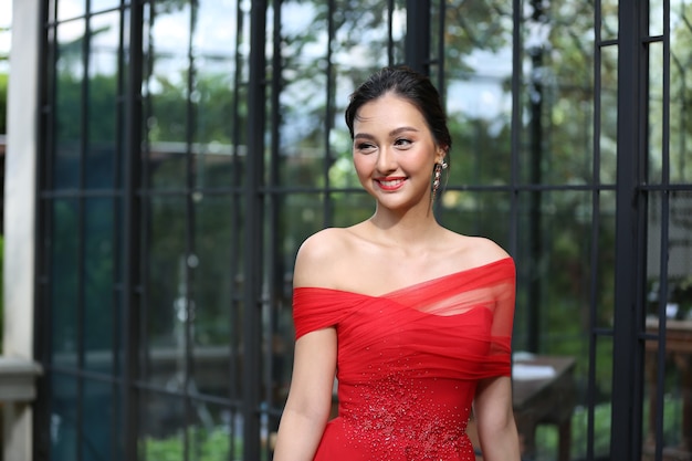 Foto mujer asiática joven en un vestido rojo hermoso que mira la cámara con una sonrisa. modelo de moda, concepto de novia o preboda.