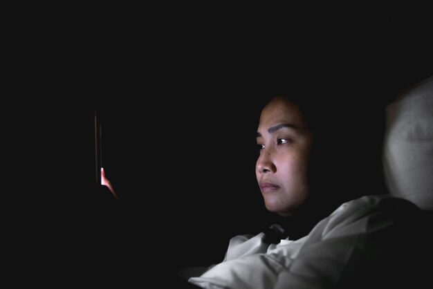 Mujer asiática juega al teléfono inteligente en la cama por la noche Noticias tailandesas adictas a la gente sobre COVID19 Hasta que no puede dormir