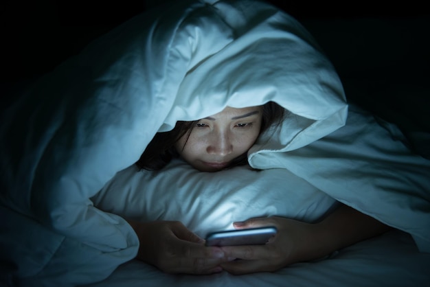 Mujer asiática juega al teléfono inteligente en la cama por la nocheGente de Tailandia