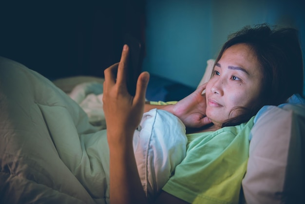 Mujer asiática juega al teléfono inteligente en la cama por la nocheGente de TailandiaAdicto a las redes socialesJuega a internet toda la noche