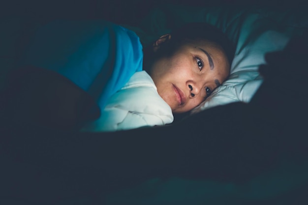 Mujer asiática juega al teléfono inteligente en la cama por la nocheGente de TailandiaAdicto a las redes socialesJuega a internet toda la nocheLychnobite