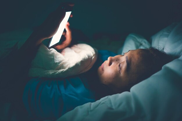 Mujer asiática juega al teléfono inteligente en la cama por la nocheGente de TailandiaAdicto a las redes socialesJuega a internet toda la nocheLychnobite