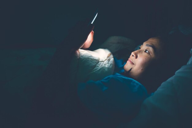 Mujer asiática juega al teléfono inteligente en la cama por la nocheGente de TailandiaAdicto a las redes socialesJuega a internet toda la nocheLychnobite