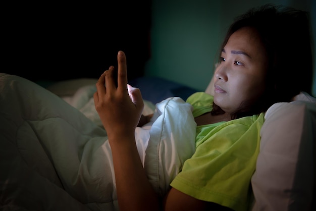 Mujer asiática juega al teléfono inteligente en la cama por la nocheGente de TailandiaAdicto a las redes socialesJuega a internet toda la nocheLychnobite