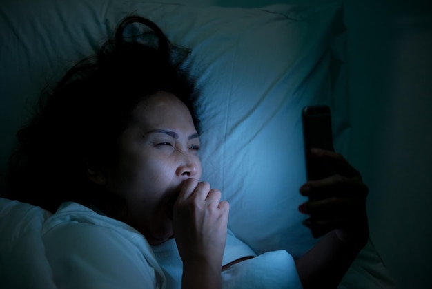 Mujer asiática jugando en el teléfono inteligente en la cama por la nocheGente tailandesaAdicto a las redes sociales