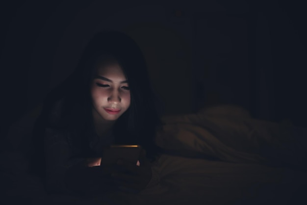 Mujer asiática jugando en el teléfono inteligente en la cama por la nocheGente tailandesaAdicto a las redes sociales