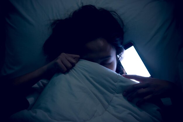 Mujer asiática jugando en el teléfono inteligente en la cama por la nocheGente tailandesaAdicto a las redes sociales