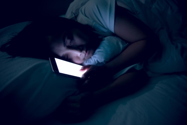 Mujer asiática jugando en el teléfono inteligente en la cama por la nocheGente tailandesaAdicto a las redes sociales