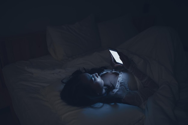 Mujer asiática jugando en el teléfono inteligente en la cama por la nocheGente tailandesaAdicto a las redes sociales