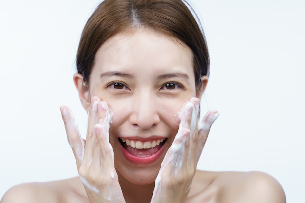 Mujer asiática lavarse la cara con espuma limpiadora de burbujas aislada en blanco.