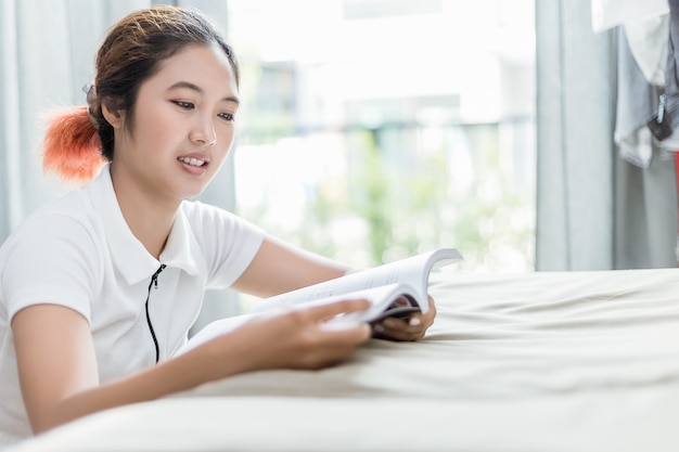 La mujer asiática lee un libro análogo en el sofá.