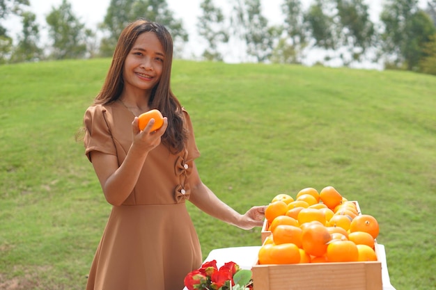 Mujer asiática levantando una canasta de naranjas en un campo