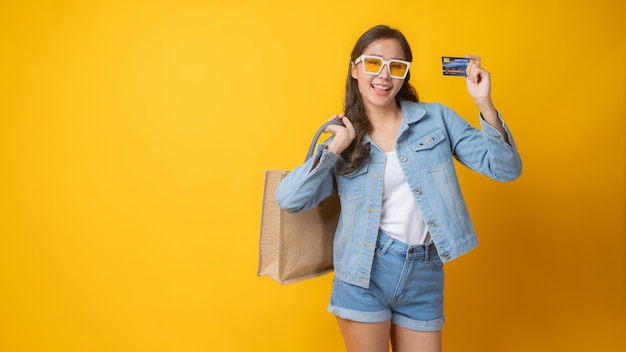 Mujer asiática linda y hermosa con gafas blancas en jeans post con tarjeta de crédito