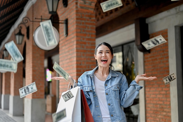 Mujer asiática llena de alegría y despreocupada llevando sus bolsas de compras y vomitando dinero