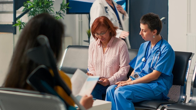 Foto mujer asiática llenando papeles de informes médicos con una enfermera, haciendo consultas médicas con un especialista en el vestíbulo de la sala de espera. personas que escriben documentos de formulario de chequeo antes de la cita.