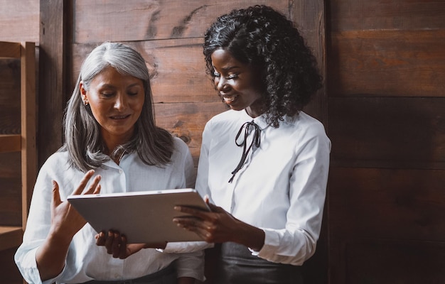 Mujer asiática madura y jóvenes empresarias africanas trabajando juntos mientras están de pie junto a la madera de ...