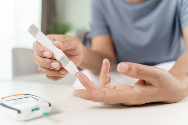 Mujer asiática madura con lanceta en el dedo para controlar el nivel de azúcar en la sangre con el medidor de glucosa, salud y medicina, diabetes, concepto de glucemia