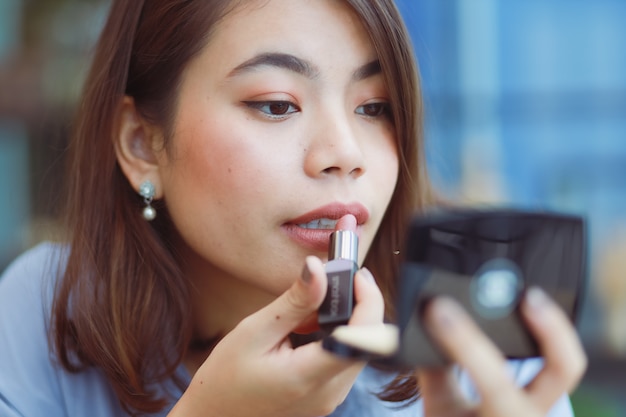 Mujer asiática maquillaje su cara con lápiz labial en café