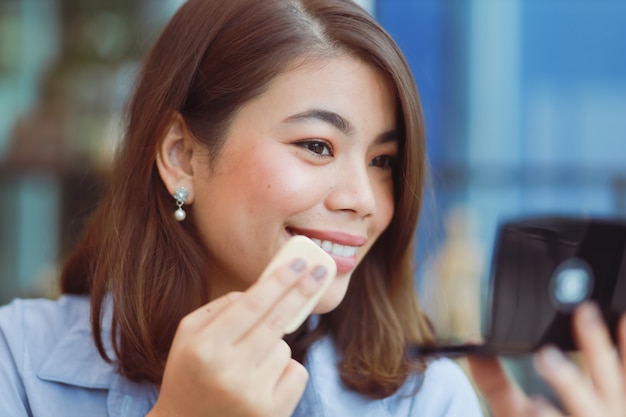 Mujer asiática maquillaje su cara con lápiz labial en café