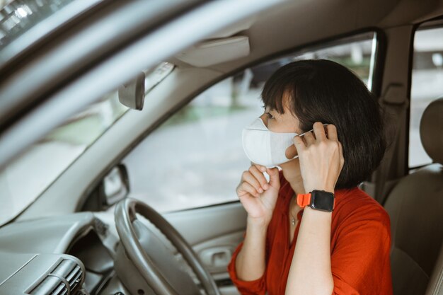 Mujer asiática en máscara protectora conduciendo un coche en la carretera. Viajar seguro.