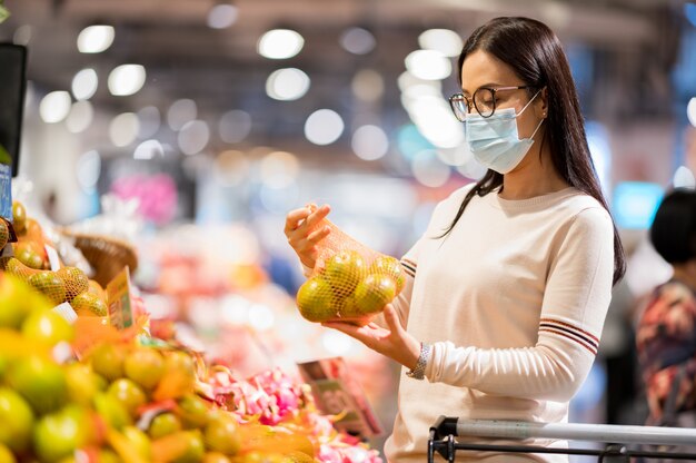 Mujer asiática con mascarilla de compras en el supermercado durante el virus corona