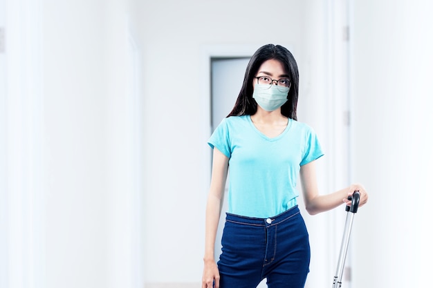 Mujer asiática con una mascarilla y gafas de pie con una maleta en el hospital. Chequeo médico antes de viajar