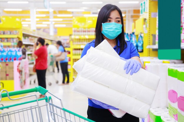 Mujer asiática en mascarilla médica y guantes médicos elegir papel higiénico en supermercado