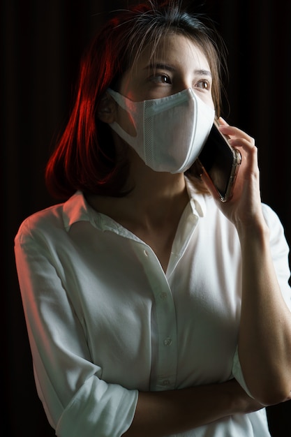 Mujer asiática con mascarilla quirúrgica haciendo una llamada telefónica.