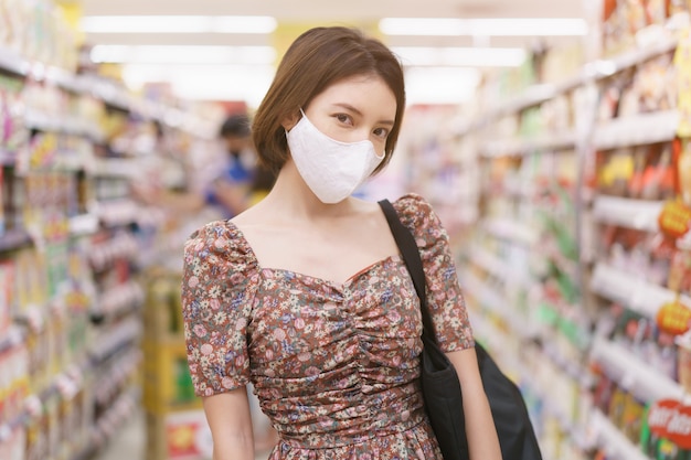 Mujer asiática con mascarilla en el supermercado durante la epidemia covid-19.