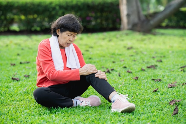 Mujer asiática mayor con dolor en el tobillo de la rodilla mientras corre en el parque Mujer asiática mayor sentada en el suelo y sosteniendo la rodilla dolorosa
